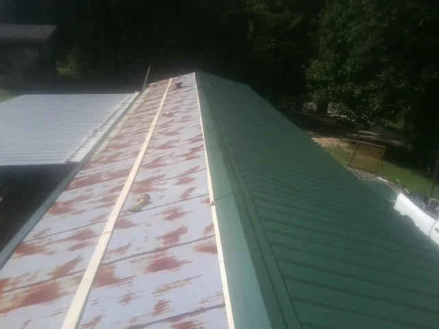 Old rusted panels beside newly installed green metal roofing — Wind Damage Roof Repair by Roofing Brothers in Avalon