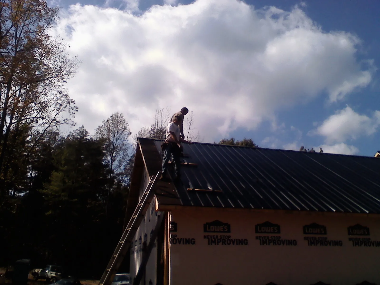 Roofer fastening dark metal panels high against a cloudy sky, from a Roof Inspection job in Avalon