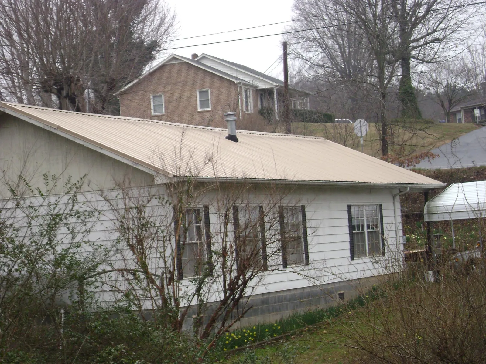Tan metal roof on a white sided house set into a hillside — Commercial Roofing by Roofing Brothers in Avalon